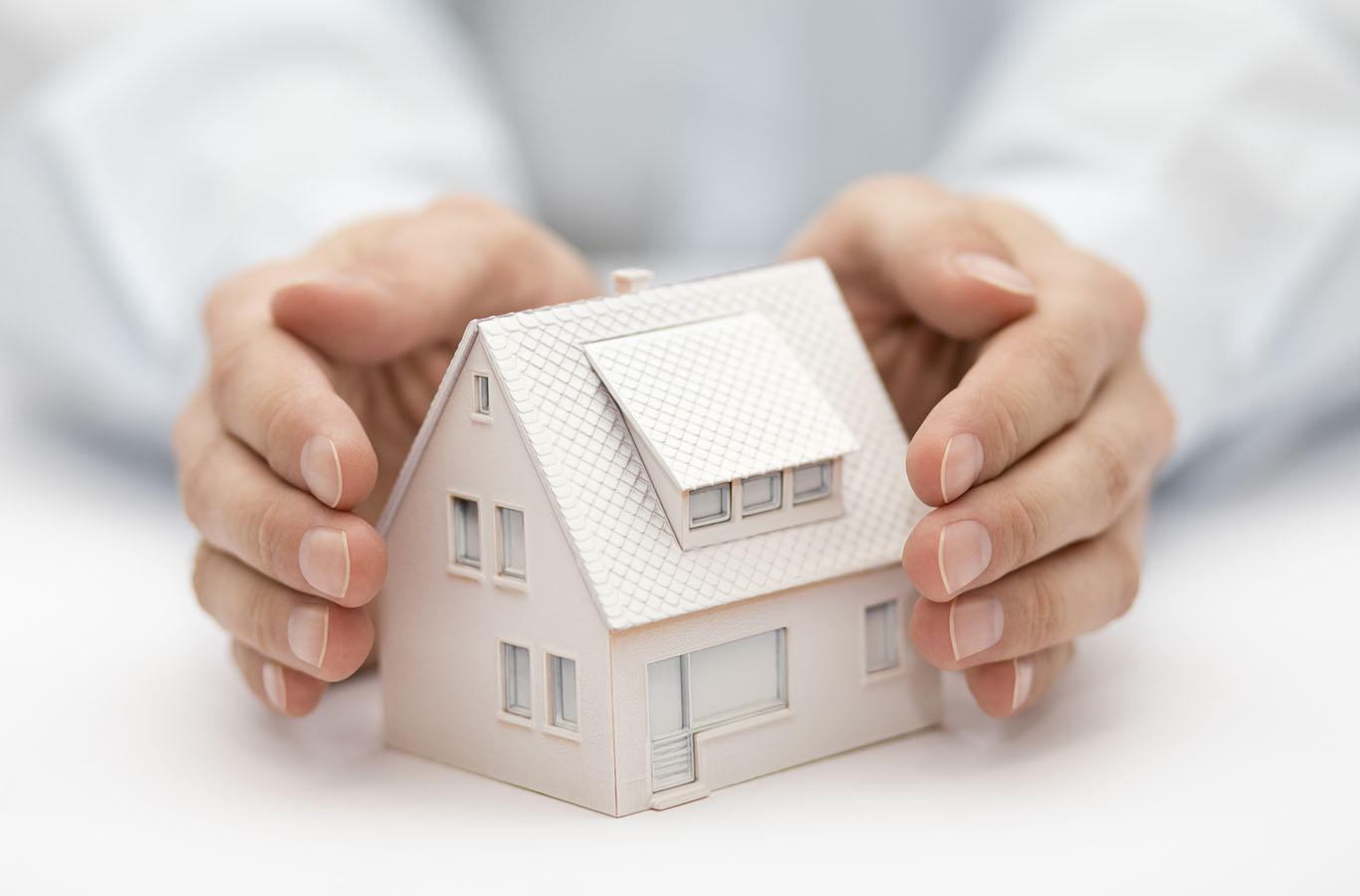 Property insurance. House miniature covered by hands.
